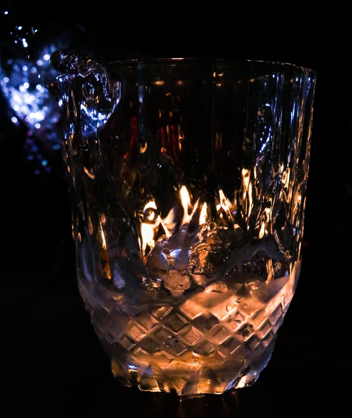 A cut-glass tumbler glowing with firelight against a black background