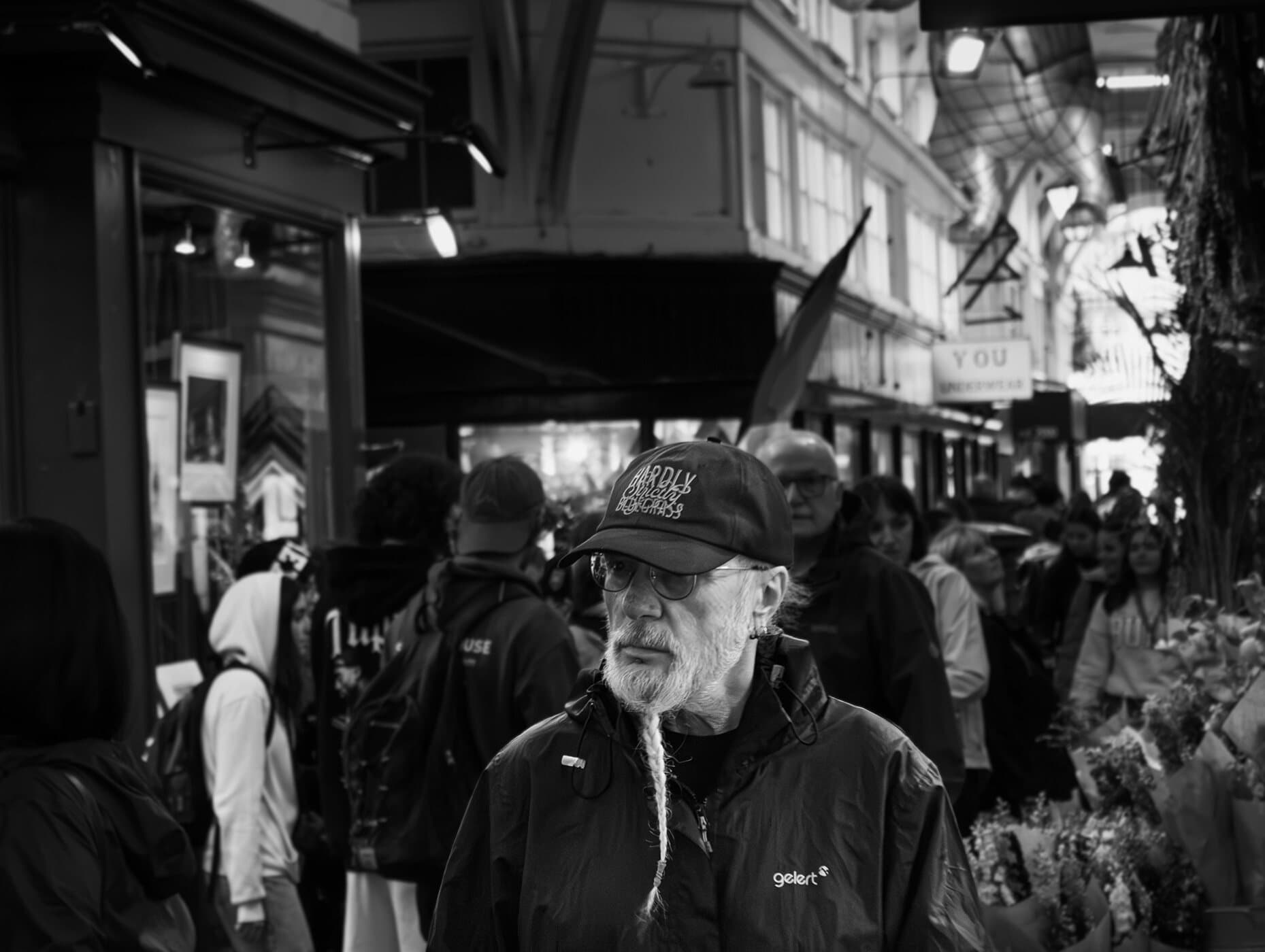 Black-and-white street market, an older man in a cap walking through the crowd