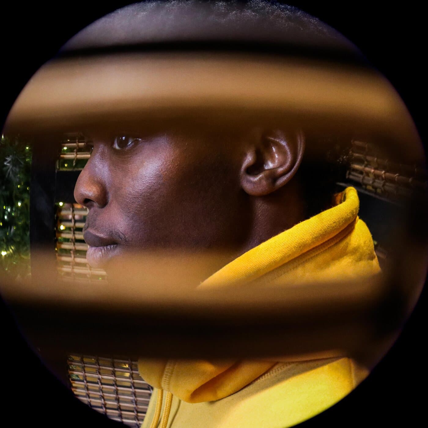 A young man in a yellow hoodie, his profile framed through a ring of warm light