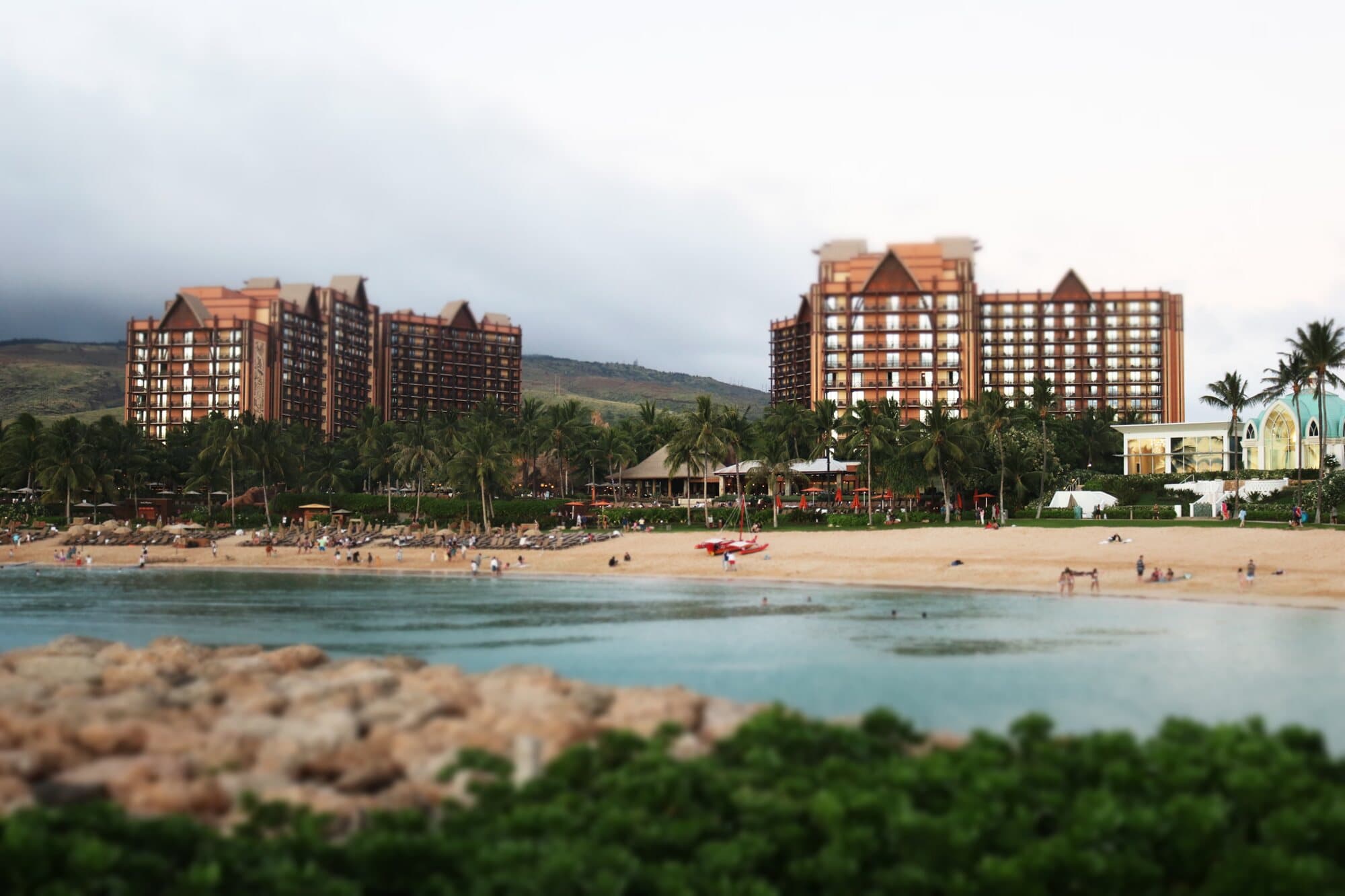Resort towers above a beach and lagoon, a rocky shore in the foreground