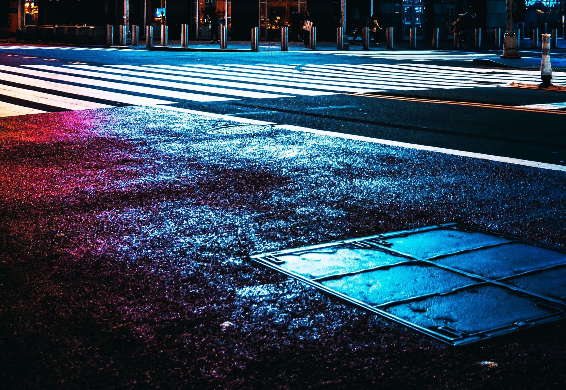 A Manhattan crosswalk at night, graded in cool blue with a red glow across the tarmac