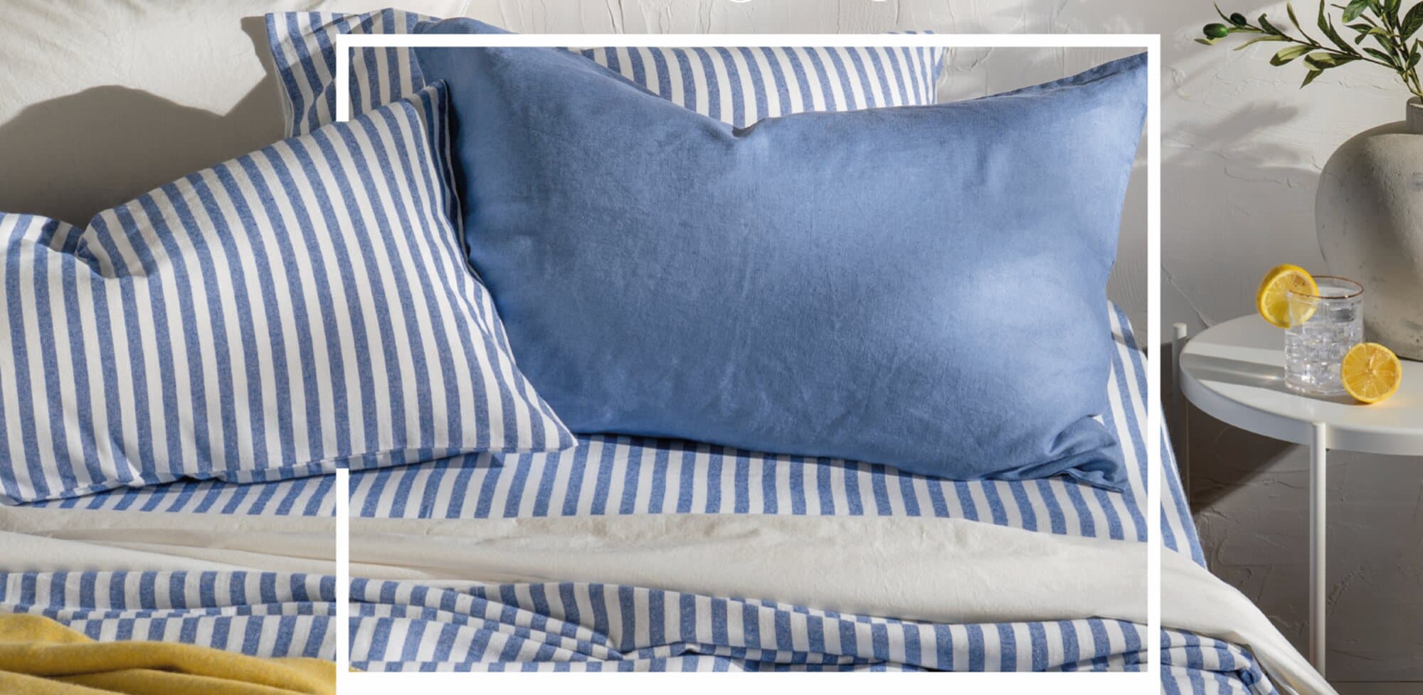Blue striped bedding and a chambray pillow inside a white frame, lemons on the bedside table